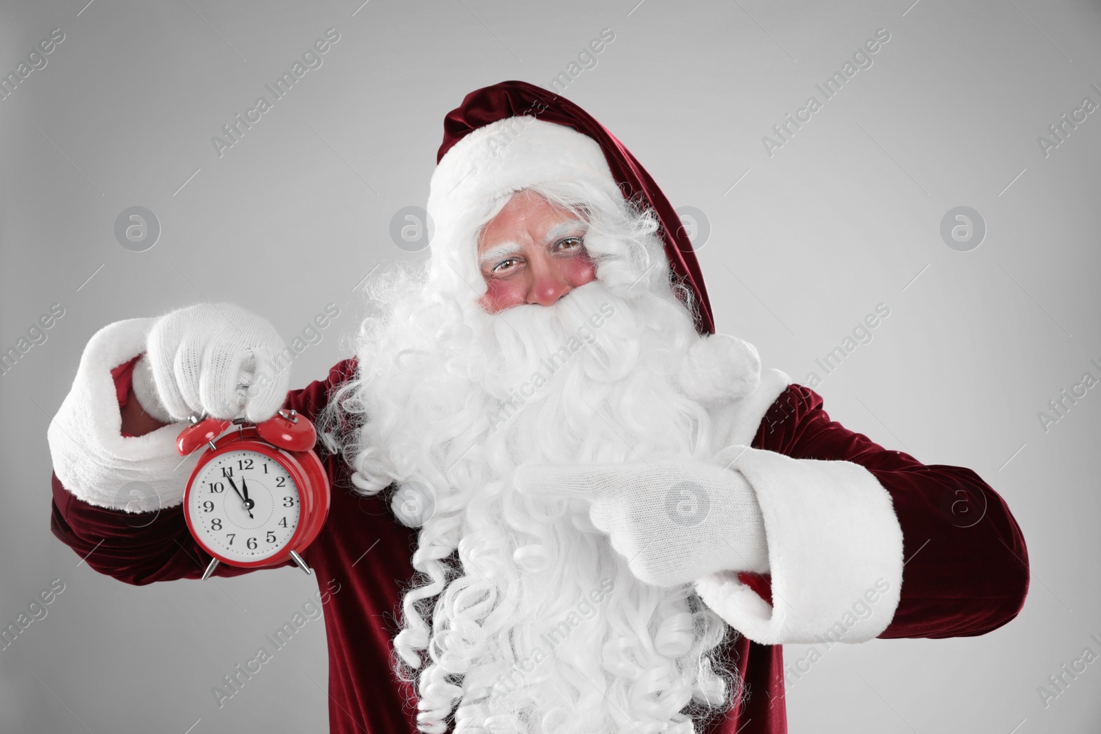 Photo of Santa Claus holding alarm clock on light grey background. Christmas countdown