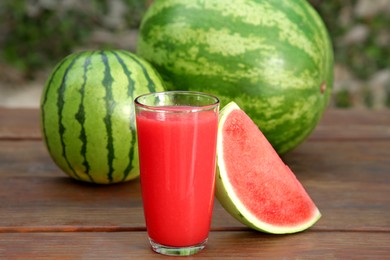 Delicious ripe watermelons and glass of fresh juice on wooden table outdoors