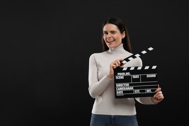 Happy actress with clapperboard on black background, space for text. Film industry