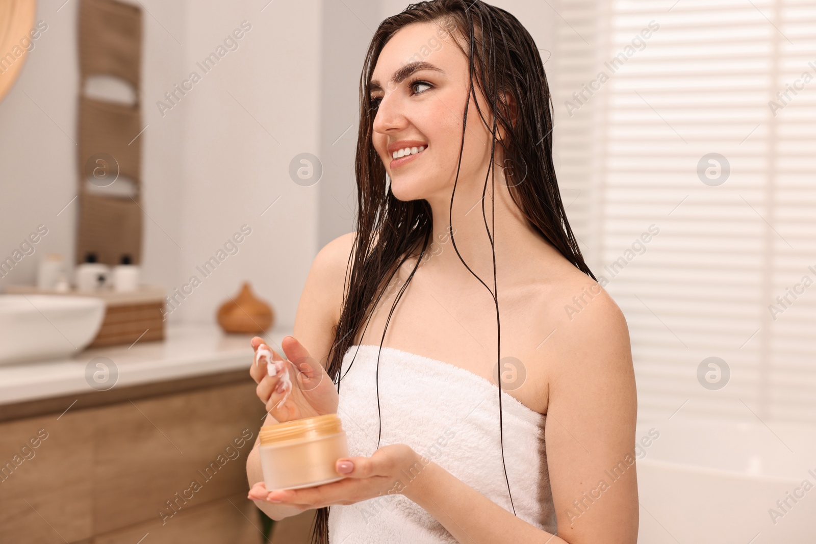 Photo of Young woman with jar of hair mask in bathroom