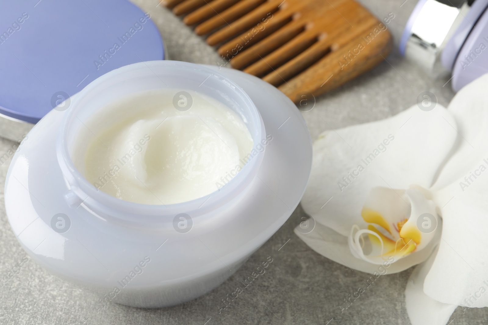 Photo of Jar of hair care cosmetic product, orchid flower and comb on grey table, closeup