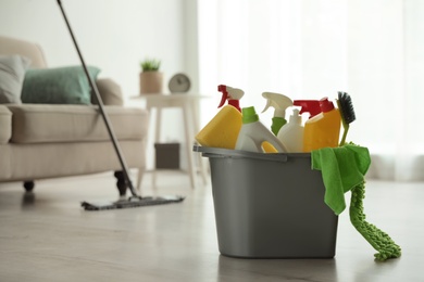 Photo of Bucket with different cleaning supplies on floor indoors. Space for text