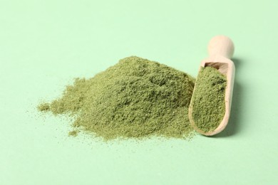 Photo of Pile of wheat grass powder and scoop on green table