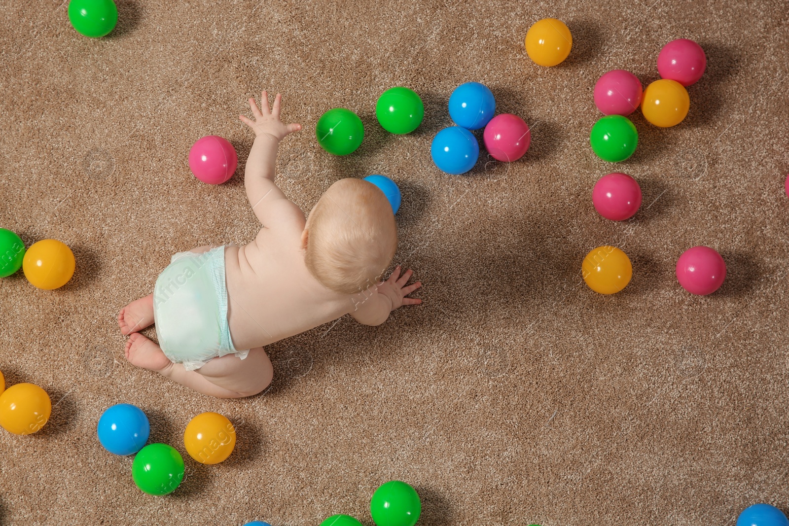 Photo of Cute little baby crawling on carpet with toys, top view