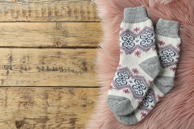 Photo of Knitted socks and pink faux fur on wooden table, flat lay. Space for text