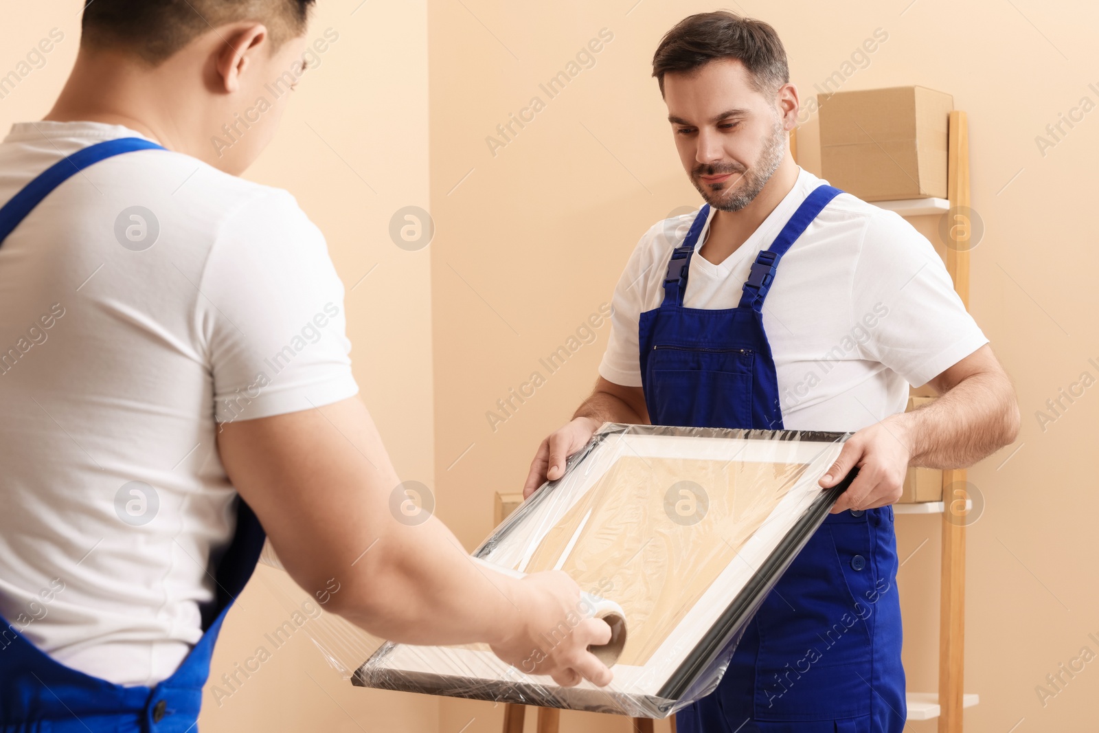 Photo of Workers wrapping picture frame in stretch film indoors