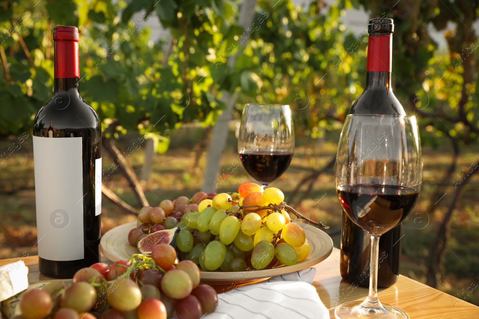 Photo of Red wine and snacks served for picnic on wooden table outdoors