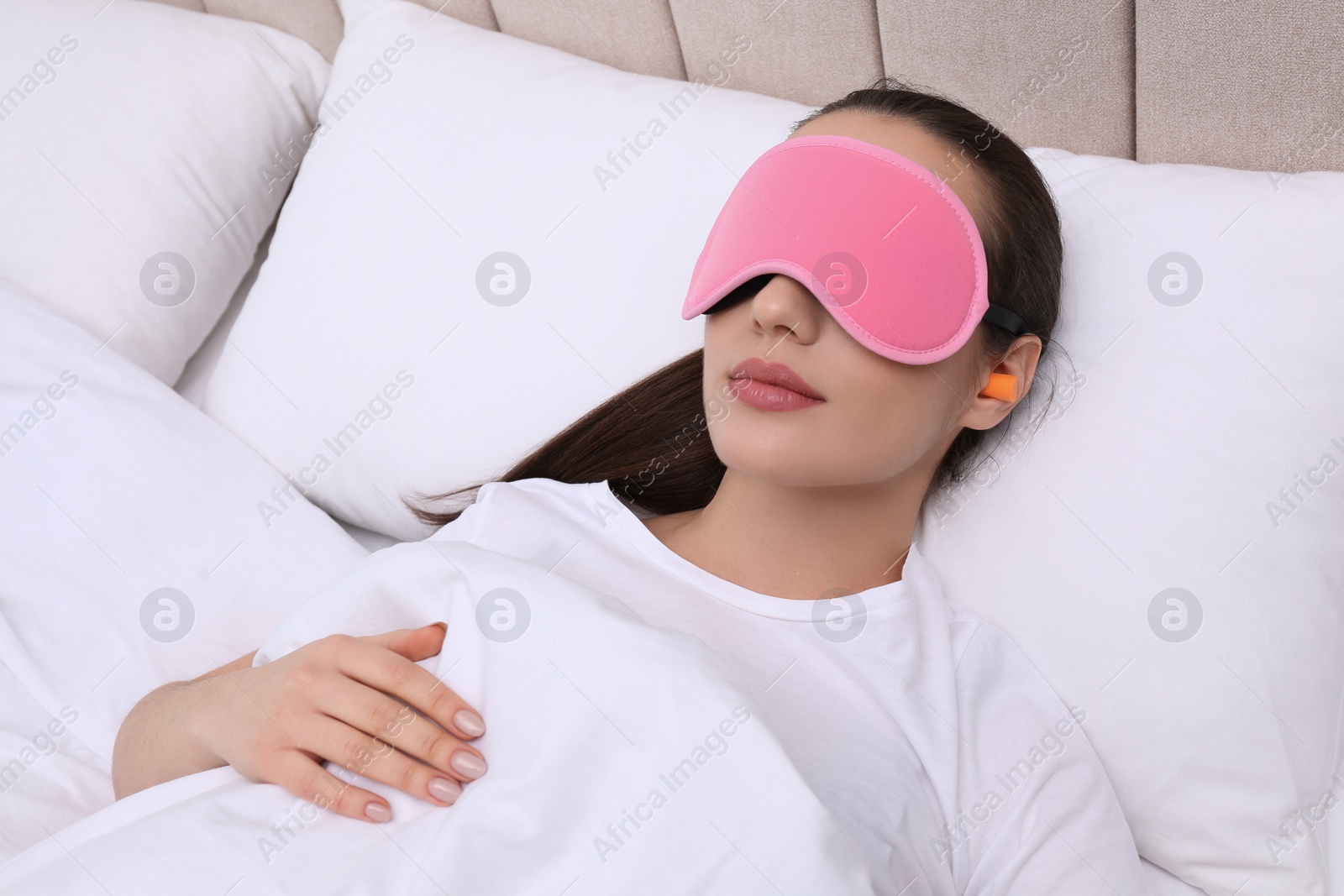 Photo of Young woman with foam ear plugs and mask sleeping in bed