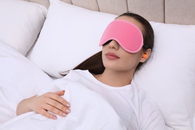Young woman with foam ear plugs and mask sleeping in bed