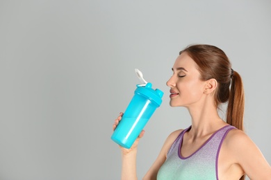 Photo of Athletic young woman drinking protein shake on light grey background. Space for text