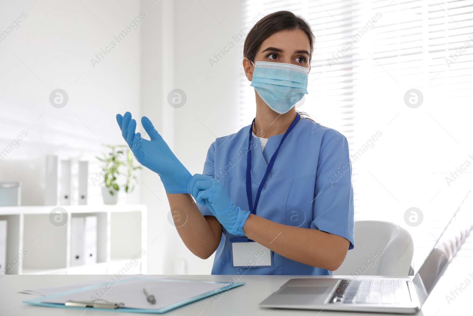 Photo of Doctor in protective mask putting on medical gloves at table in office