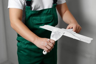 Photo of Professional worker holding putty knives with plaster indoors, closeup
