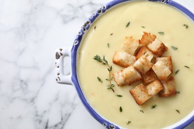 Photo of Tasty potato soup with croutons and rosemary in ceramic pot on white marble table, top view. Space for text