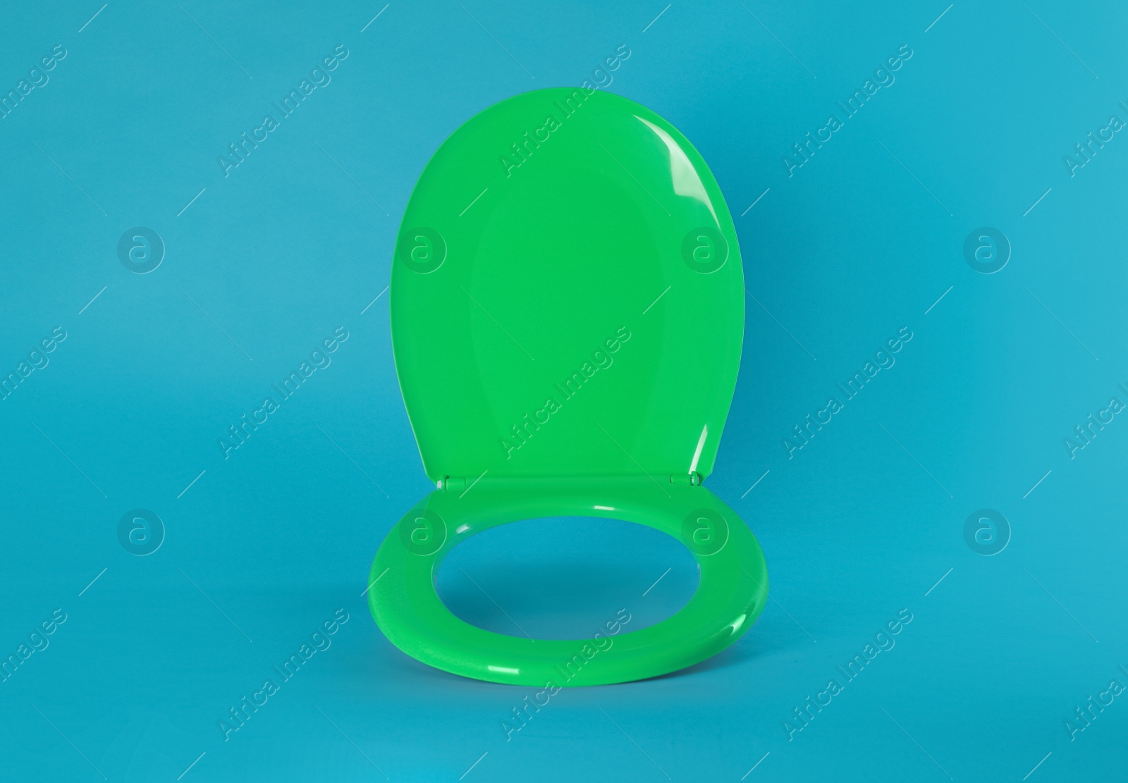 Photo of New green plastic toilet seat on light blue background, space for text