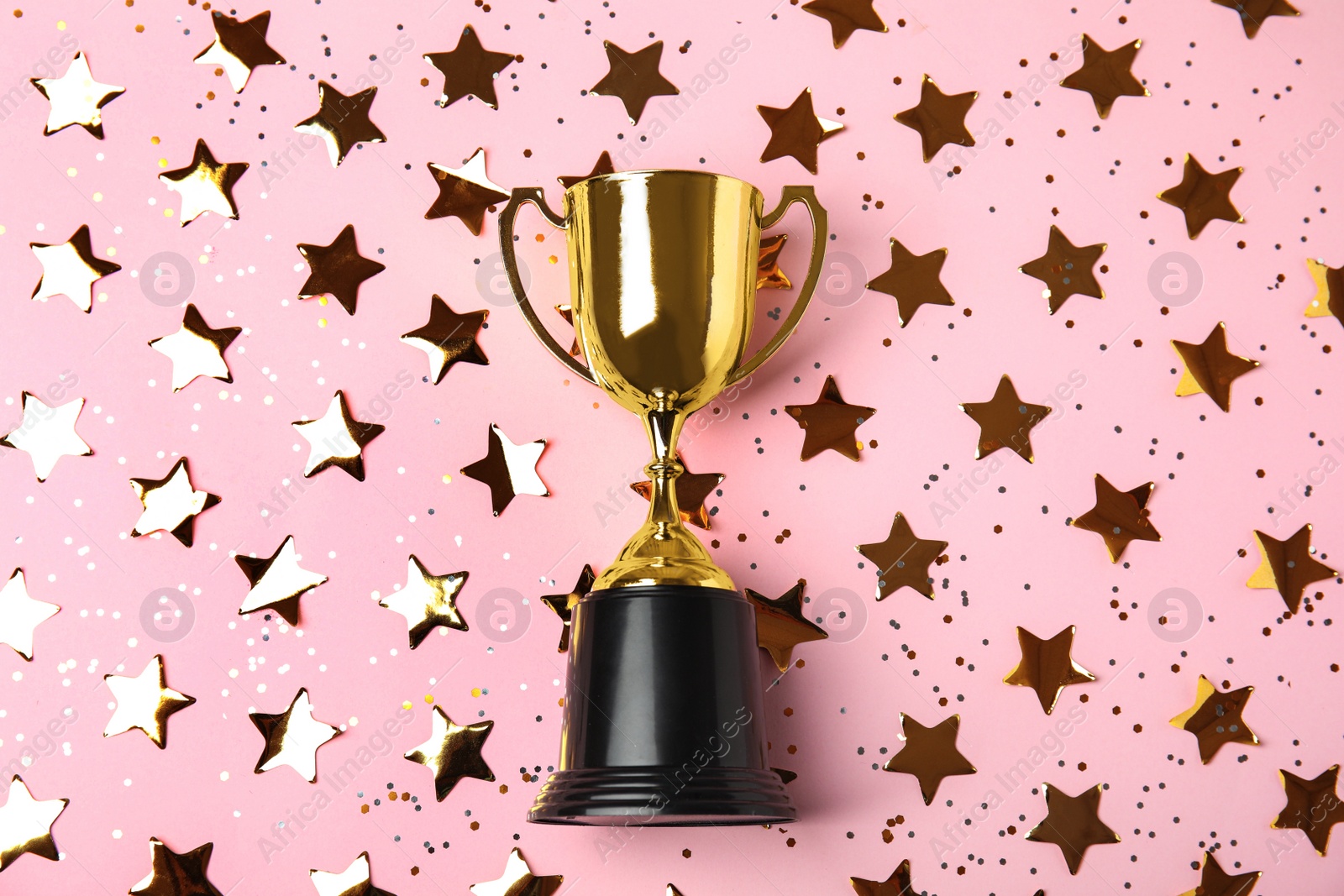 Photo of Gold trophy cup and confetti on light pink background, flat lay