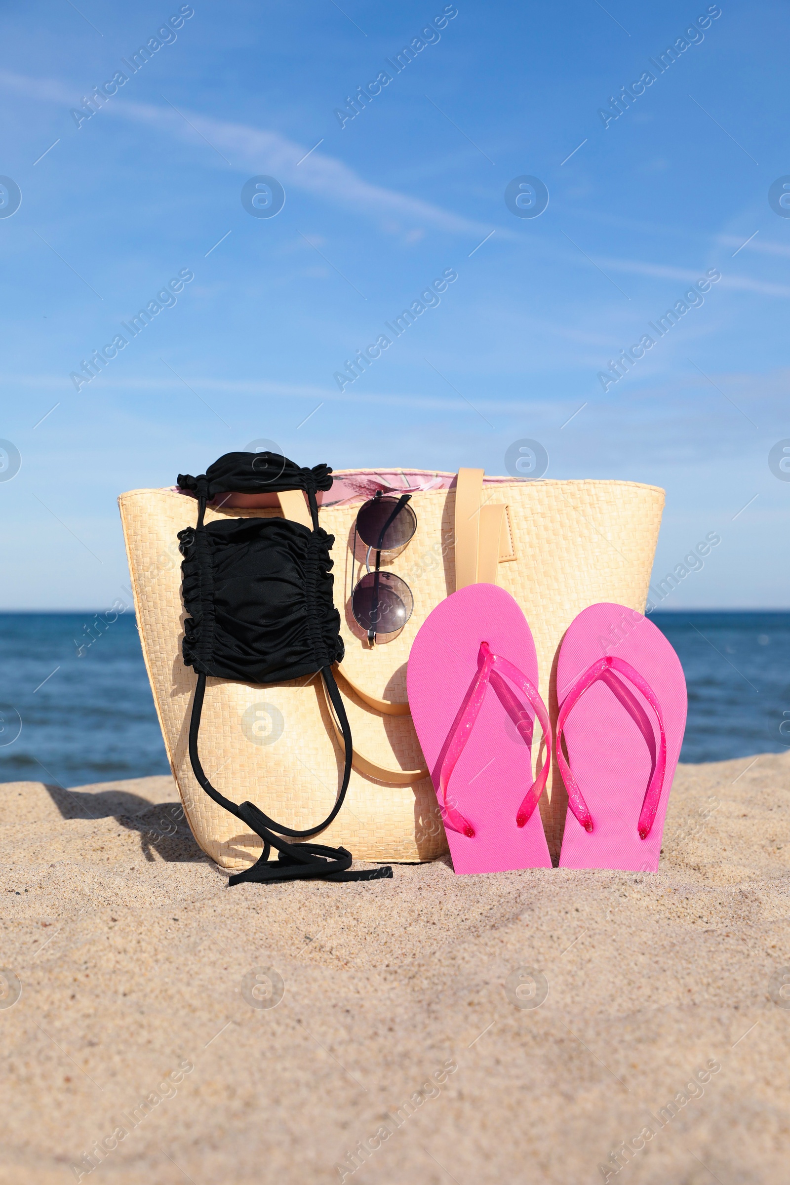 Photo of Summer bag with beach accessories on sand near sea