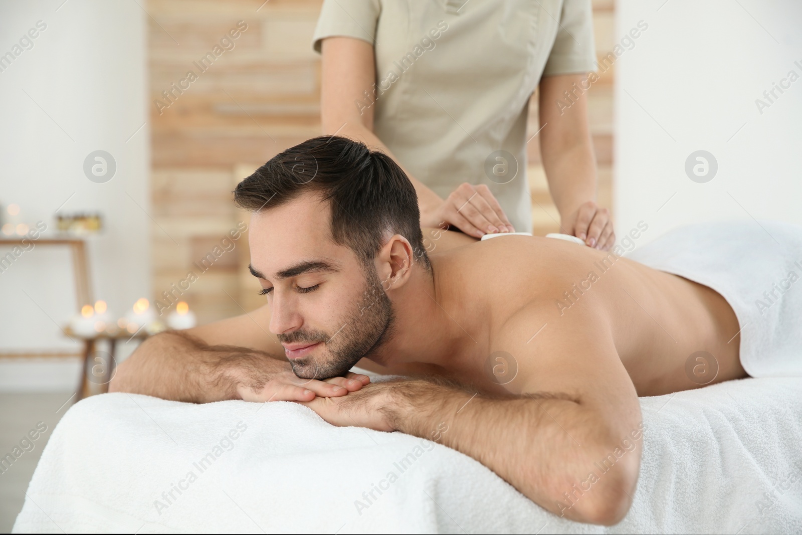 Photo of Handsome man receiving hot stone massage in spa salon