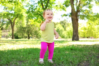 Cute baby girl learning to walk in park on sunny day