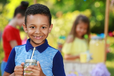 Photo of Cute little African-American boy with natural lemonade in park, space for text. Summer refreshing drink