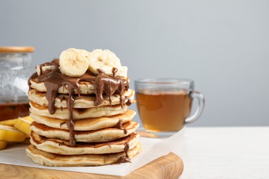 Photo of Tasty pancakes with sliced banana served on white table, space for text