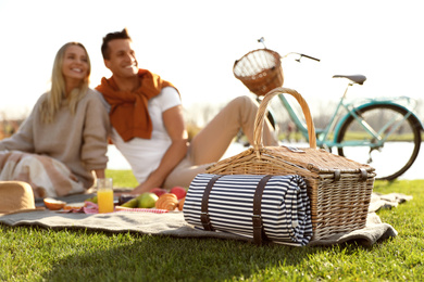 Photo of Happy young couple having picnic outdoors, focus on wicker basket