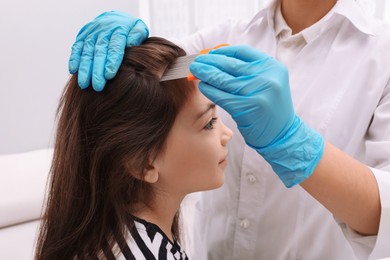 Photo of Doctor using nit comb on little girl's hair indoors. Anti lice treatment