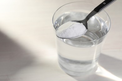 Photo of Glass of water and spoon with baking soda on light background, closeup. Space for text