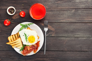 Photo of Plate with fried egg, bacon and toasts on wooden table