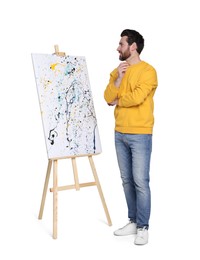 Man with brush near easel with painting on white background. Creative hobby