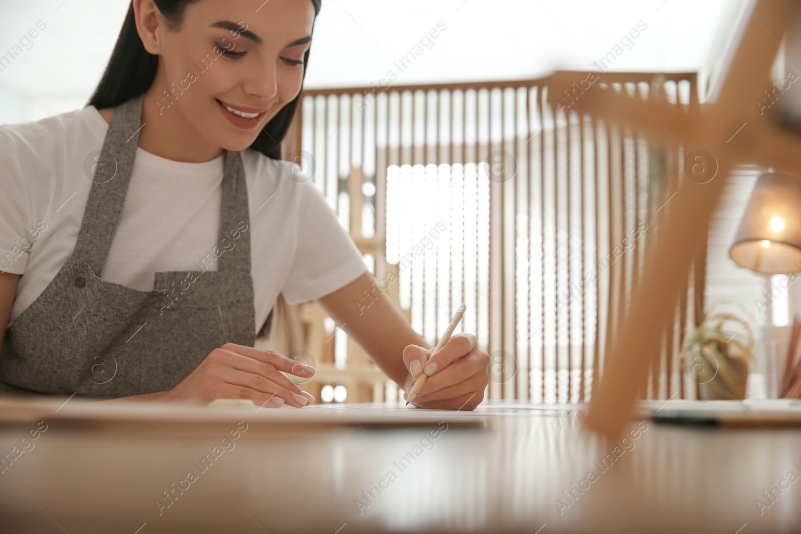 Photo of Young woman drawing with pencil at table indoors