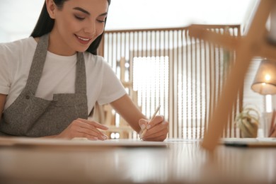 Photo of Young woman drawing with pencil at table indoors