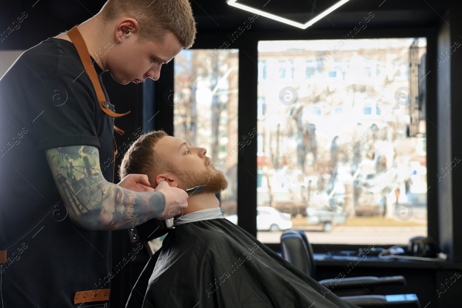 Photo of Professional hairdresser working with bearded client in barbershop