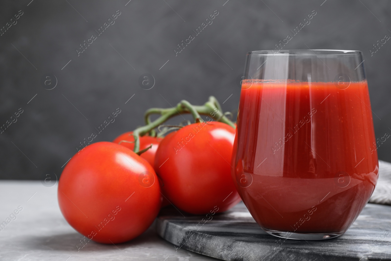 Photo of Delicious fresh tomato juice on grey marble table against black background, closeup