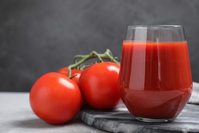 Photo of Delicious fresh tomato juice on grey marble table against black background, closeup