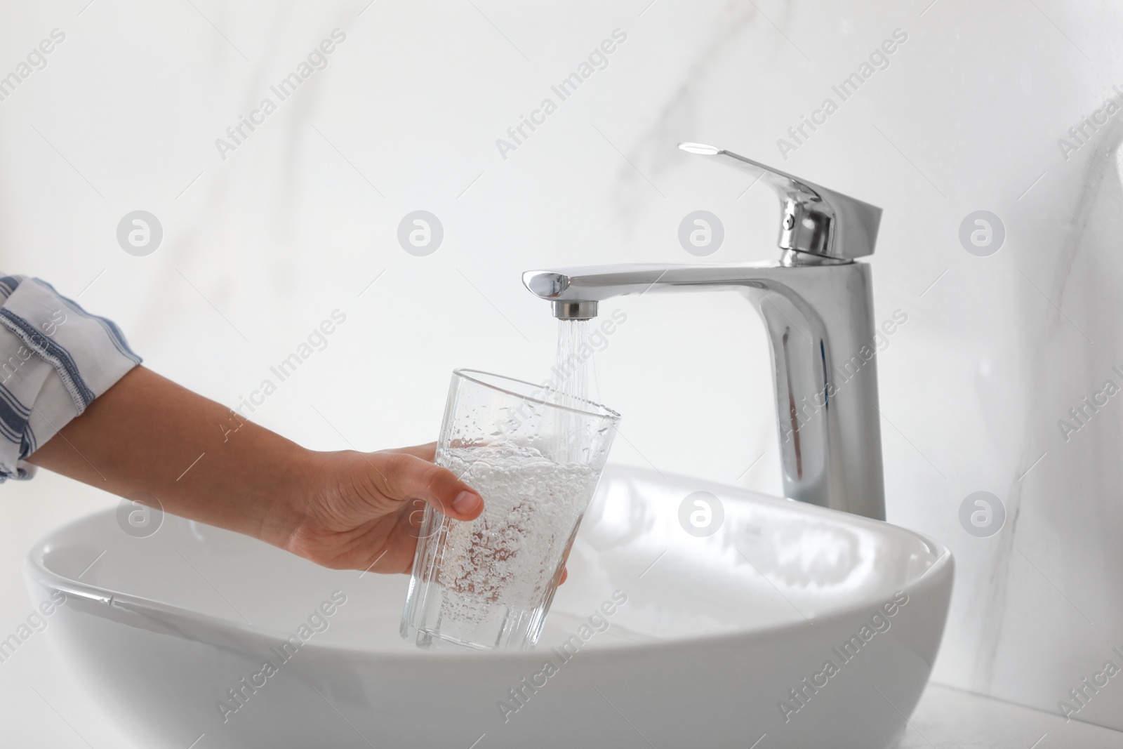 Photo of Woman filling glass with water from faucet over sink, closeup