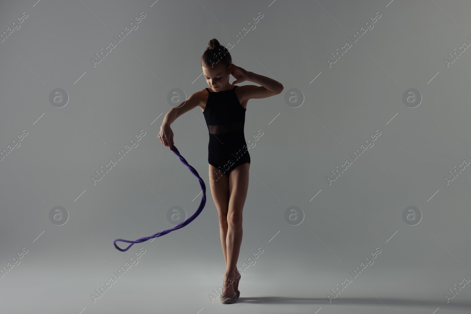 Photo of Cute little girl doing gymnastic exercise with rope on white background
