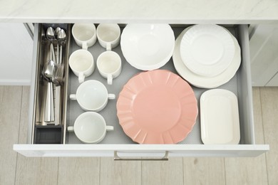 Clean plates, bowls, cups and cutlery in drawer indoors, top view