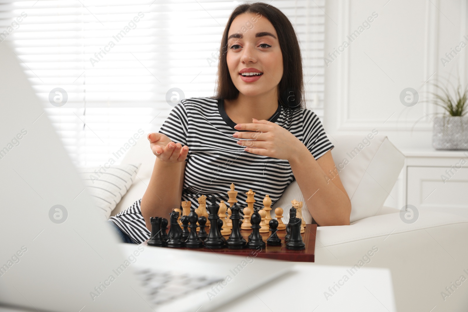 Photo of Young woman playing chess with partner through online video chat at home