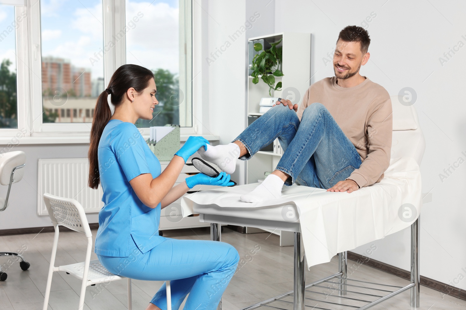 Photo of Beautiful female orthopedist fitting insole to patient's foot in hospital