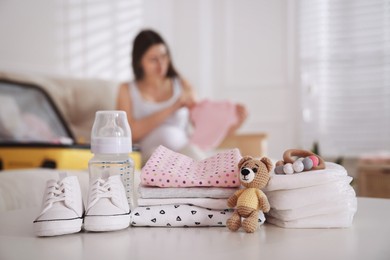 Photo of Baby clothes with accessories on white table and pregnant woman packing suitcase for maternity hospital indoors