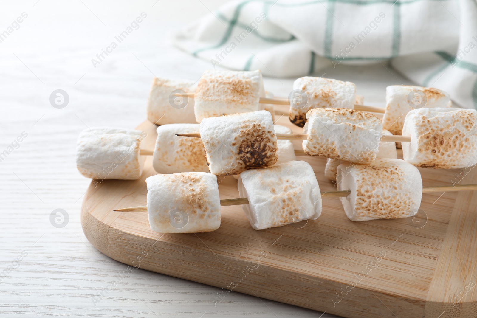 Photo of Sticks with roasted marshmallows on white wooden table, closeup