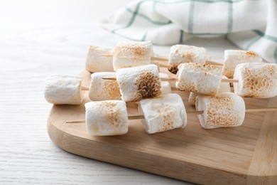 Photo of Sticks with roasted marshmallows on white wooden table, closeup