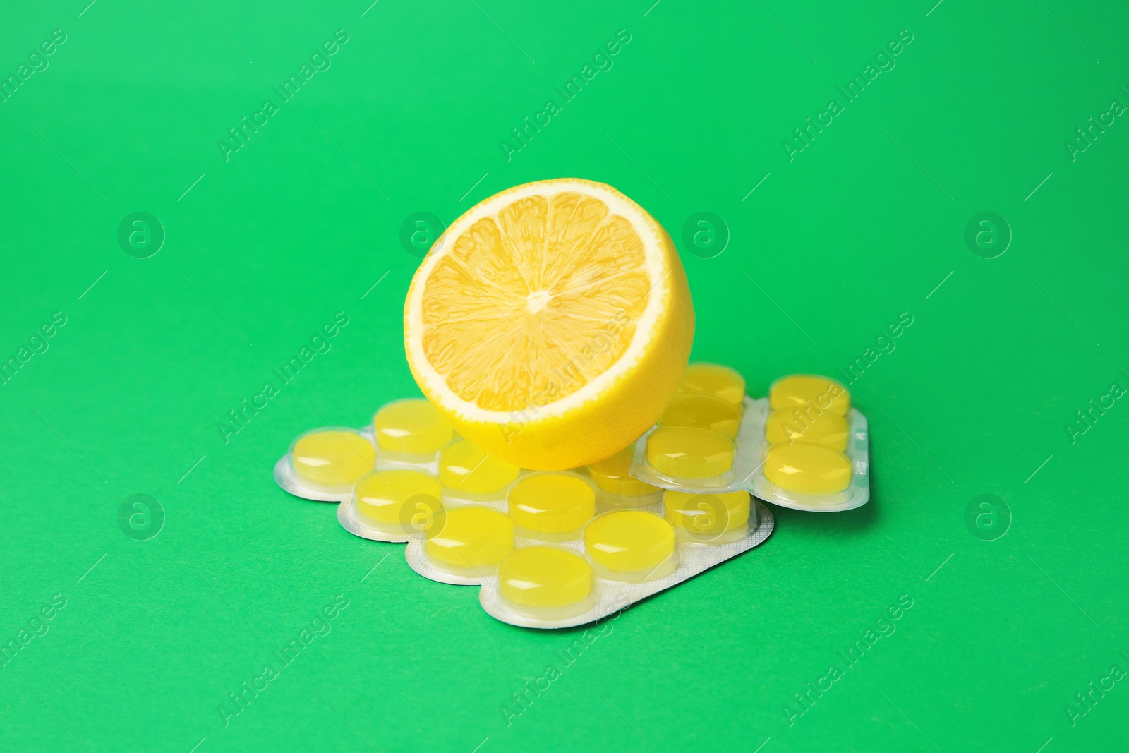 Photo of Blister with cough drops and fresh lemon on green background