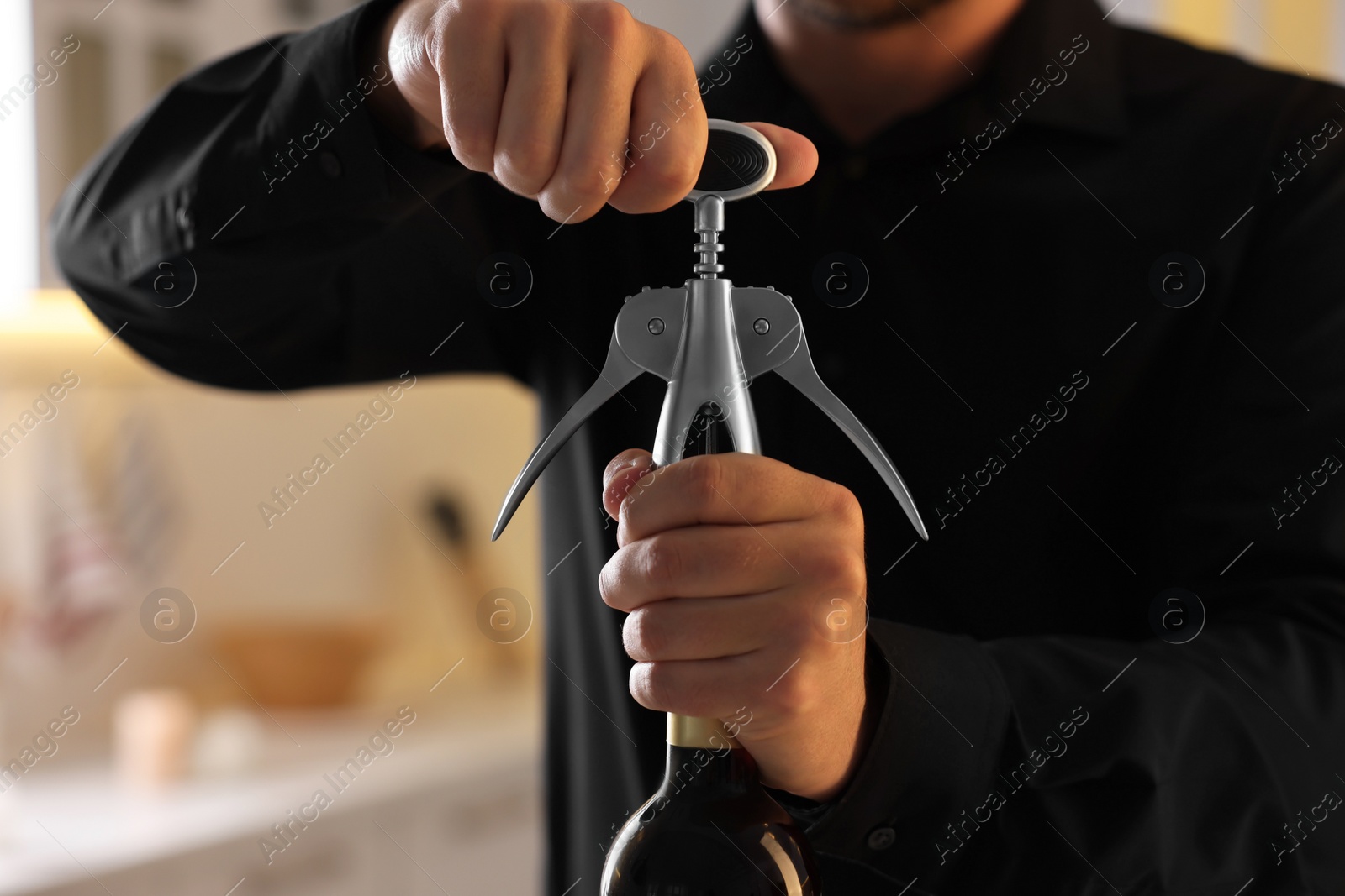 Photo of Man opening wine bottle with corkscrew indoors, closeup