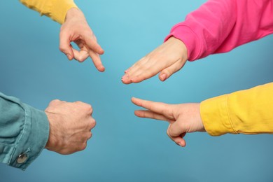 People playing rock, paper and scissors on light blue background, closeup