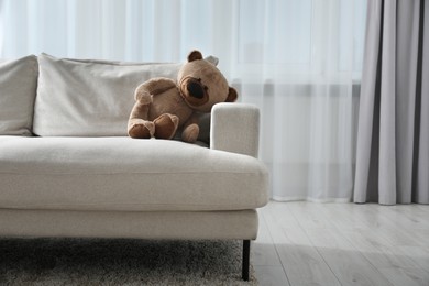 Photo of Cute lonely teddy bear on sofa in room. Space for text