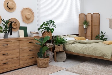 Comfortable bed and beautiful green houseplants in bedroom