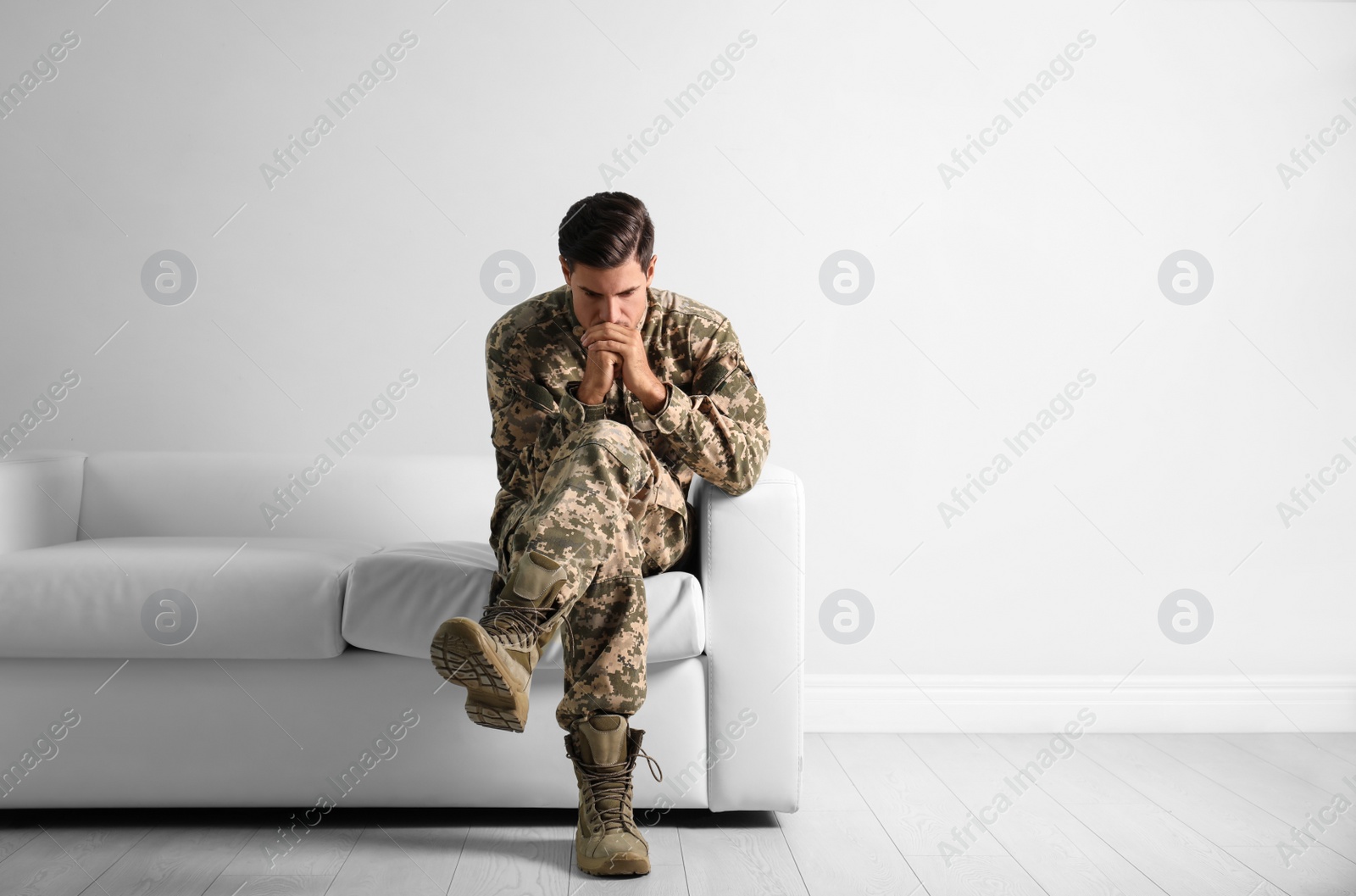 Photo of Stressed military officer sitting on sofa near white wall indoors. Space for text