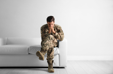 Photo of Stressed military officer sitting on sofa near white wall indoors. Space for text