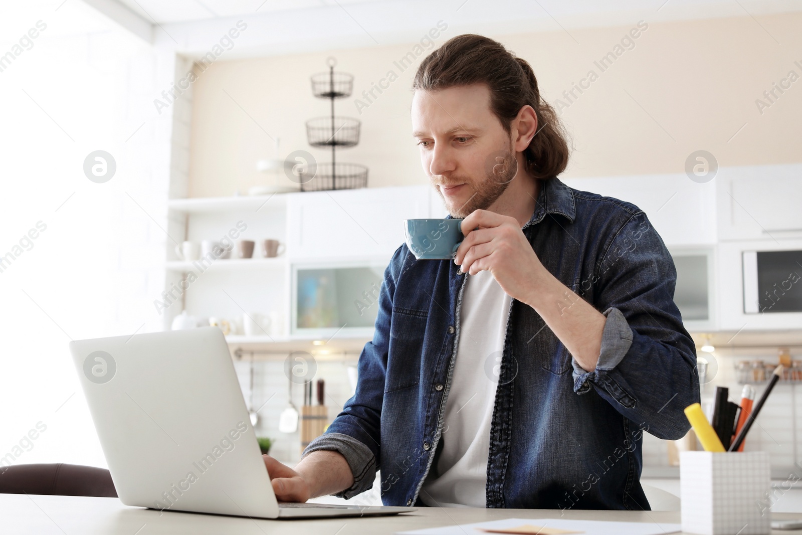 Photo of Young man working with laptop at desk in home office